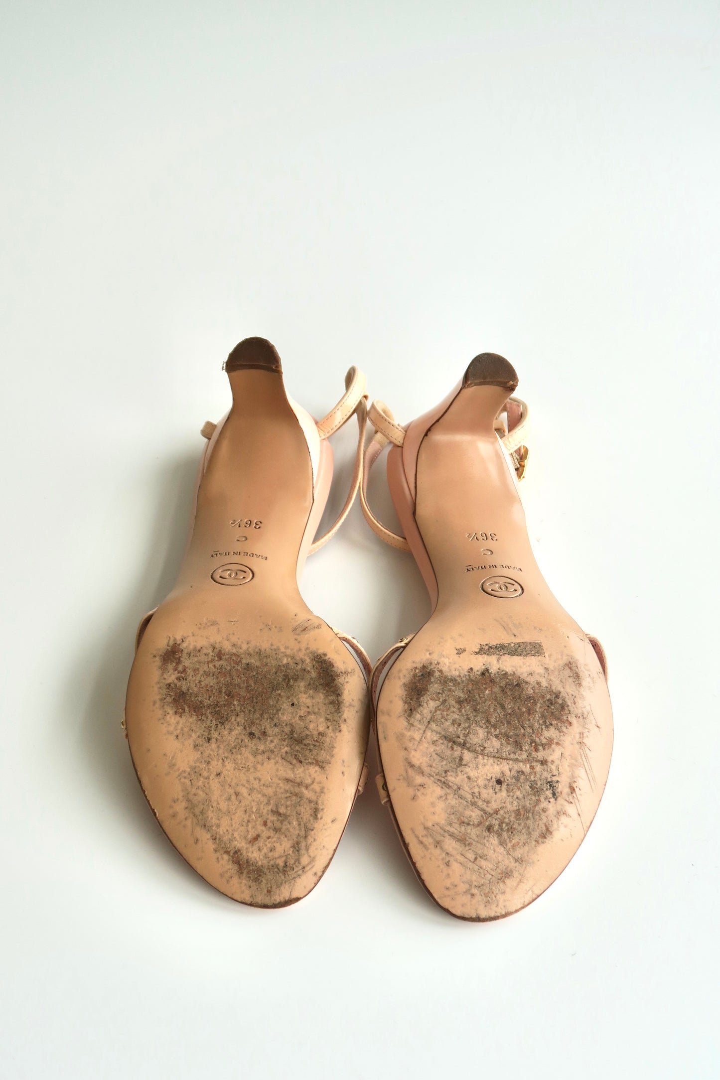 Pair of beige high-heeled shoes with soles showing signs of wear on a white background