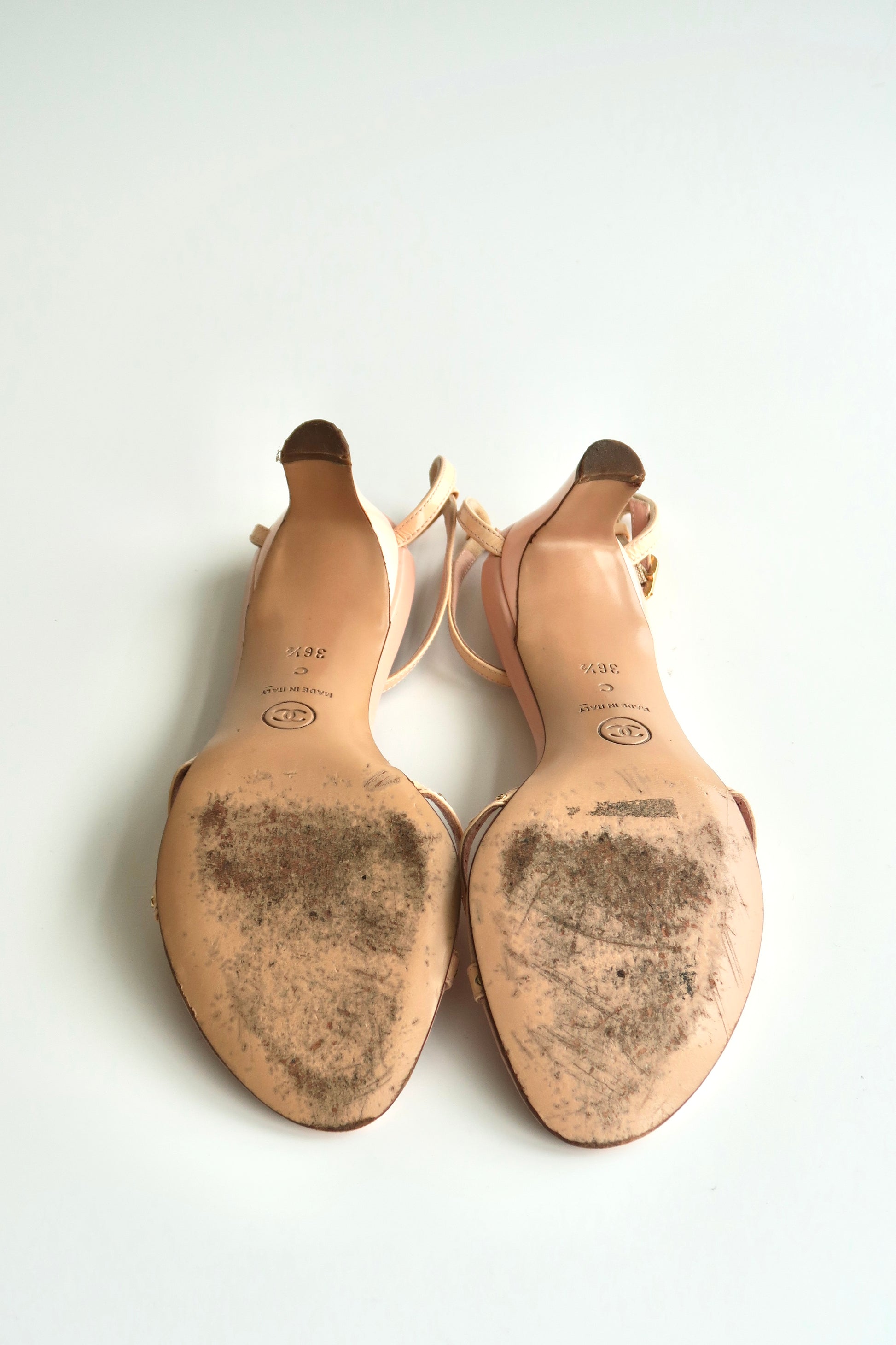 Pair of beige high-heeled shoes with soles showing signs of wear on a white background