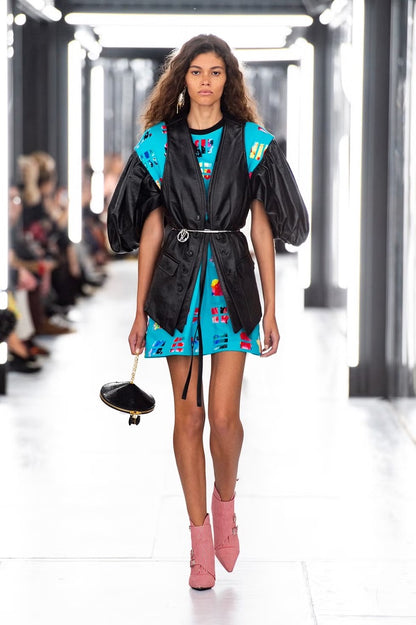 Model walking on a Louis Vuitton runway wearing a black jacket, blue dress with colorful patterns, and red and white striped boots.