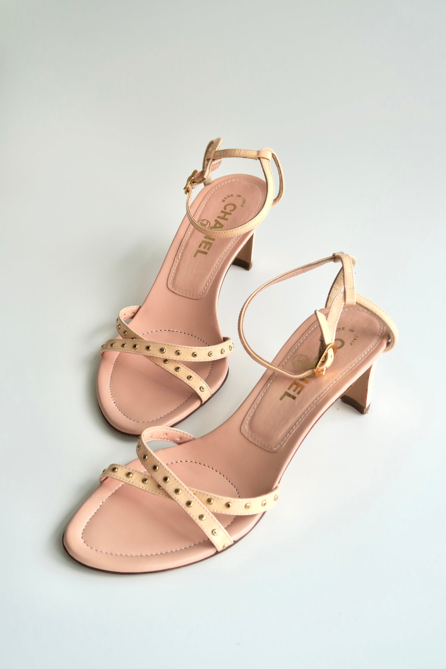 Pair of pink high-heeled sandals with gold straps on a light gray background
