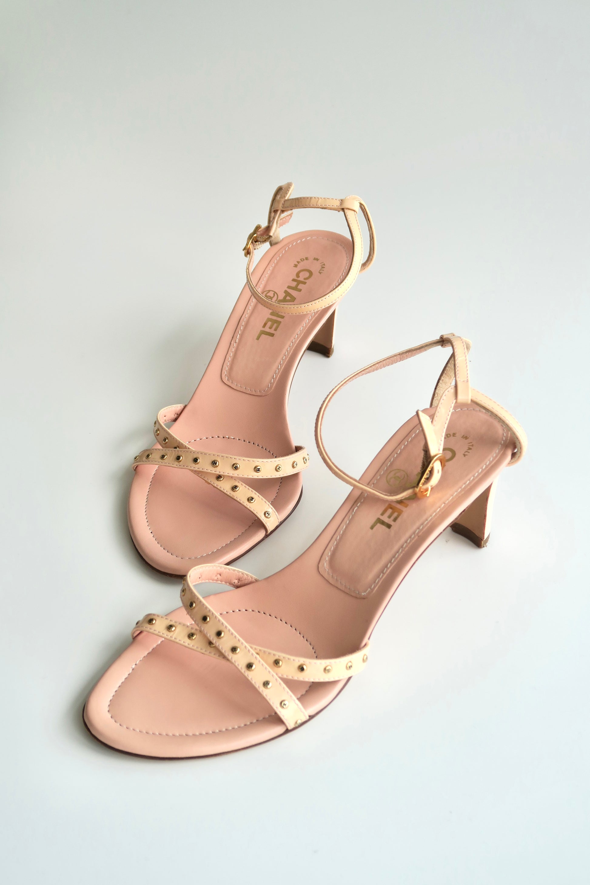 Pair of pink high-heeled sandals with gold straps on a light gray background